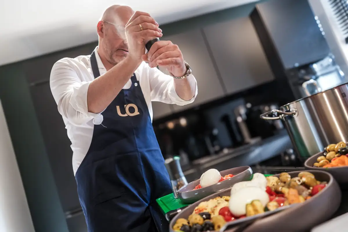 Koch mit UQ-Schürze würzt Antipasti beim Format „Chef kocht“