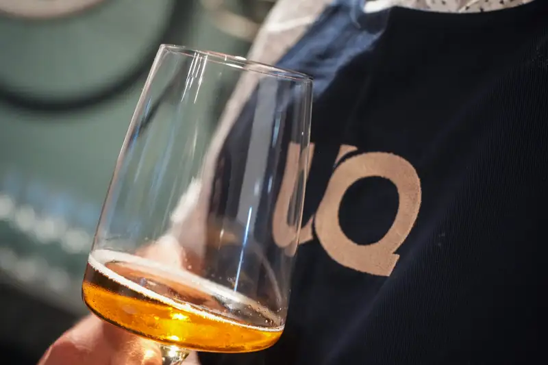 Hand mit Glas Weißwein vor UQ-Schürze im UnternehmerQuartier